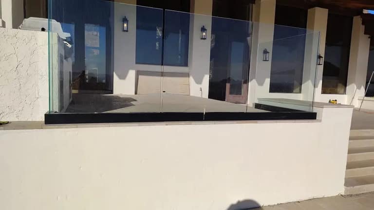 Base-mounted glass railing panels along a raised white stucco patio wall.