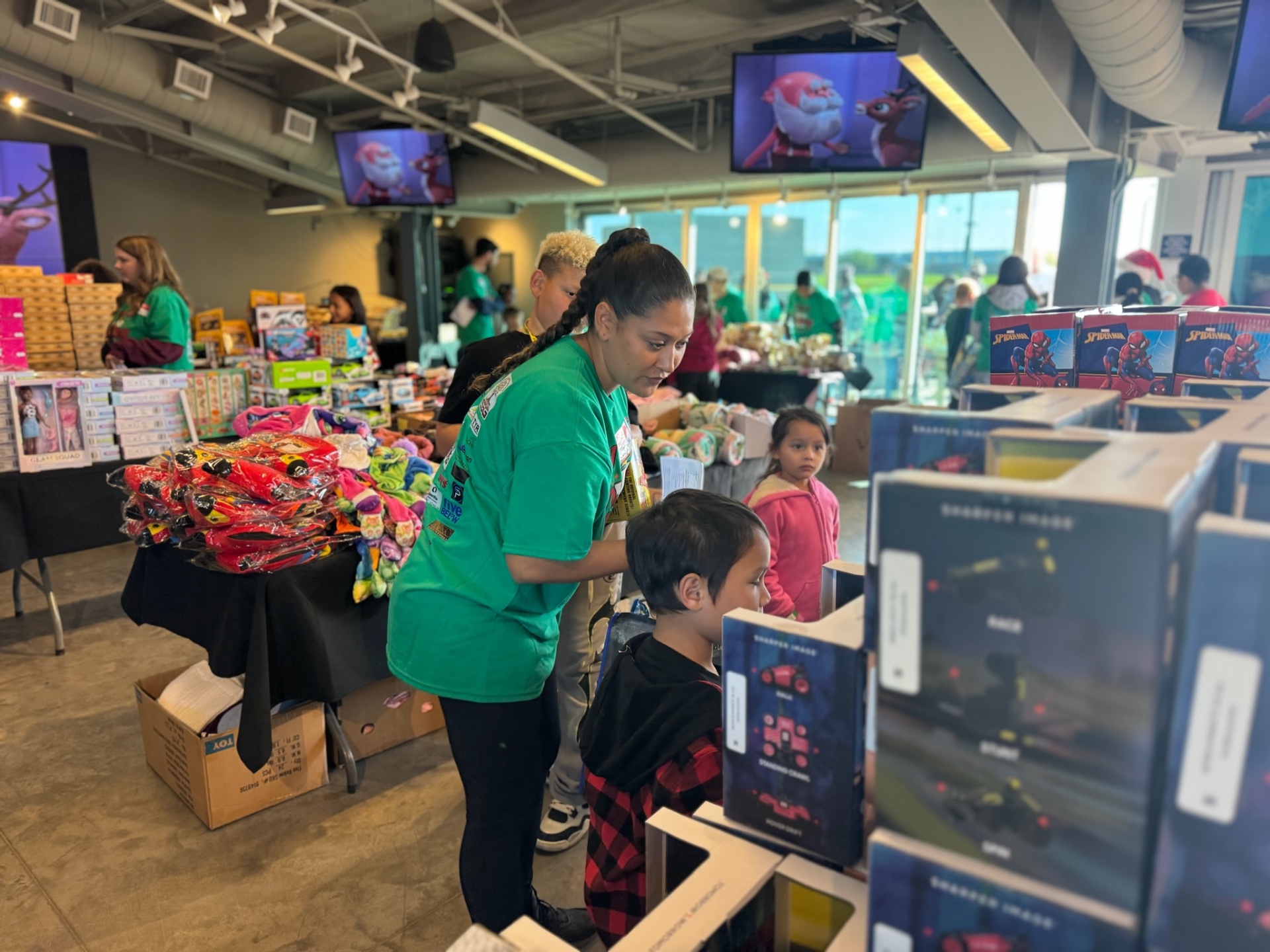 Volunteer in green Day of Giving shirt helping a family shop the toy tables at A Day of Giving 2025