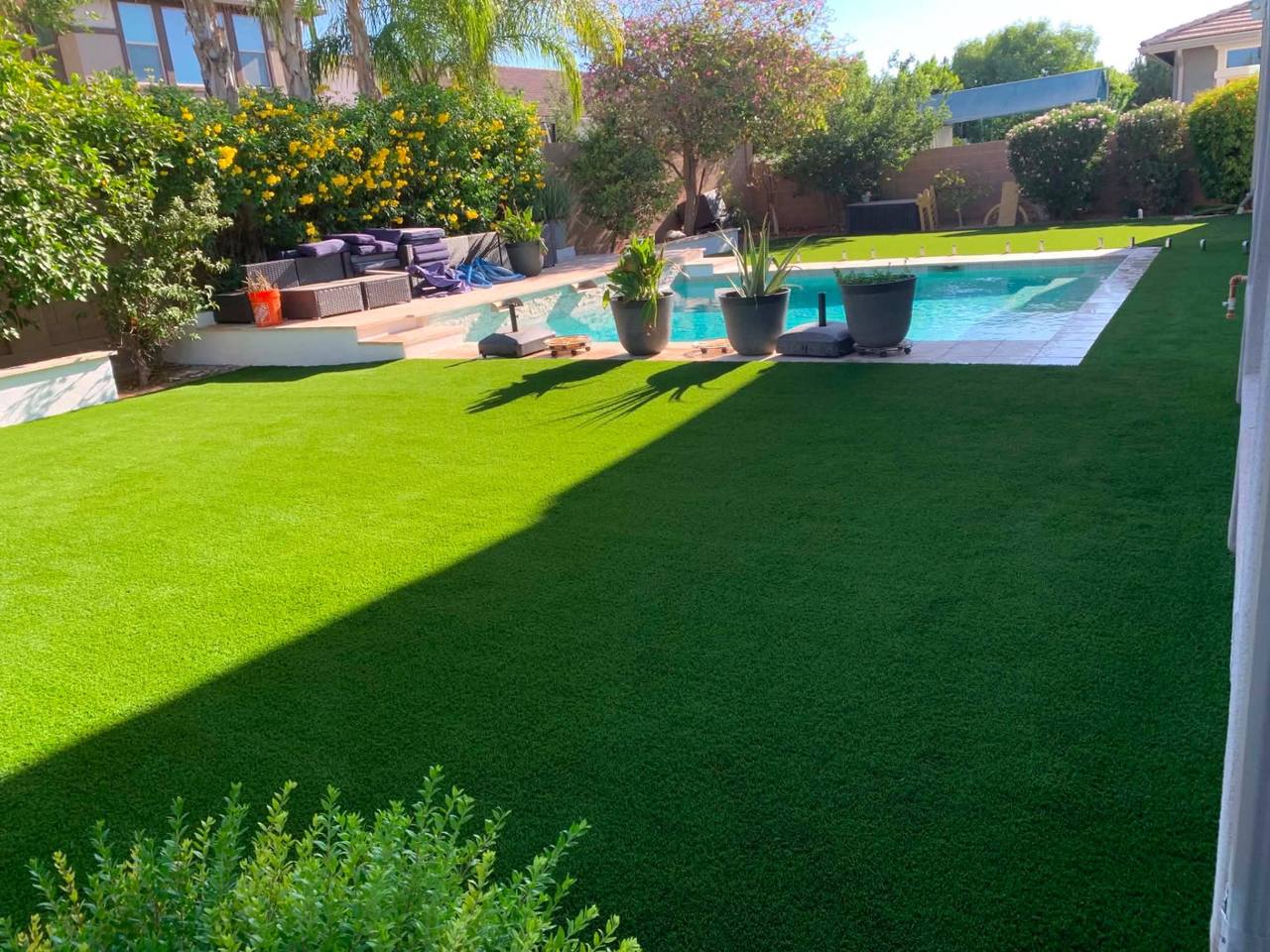 Wide turf lawn wrapping a resort pool with planters, lounge, and travertine coping.