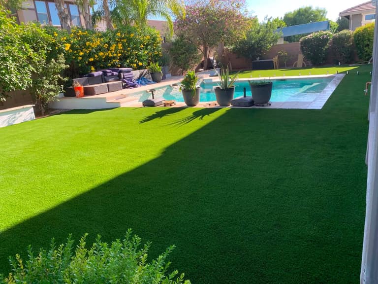 Wide turf lawn wrapping a resort pool with planters, lounge, and travertine coping.