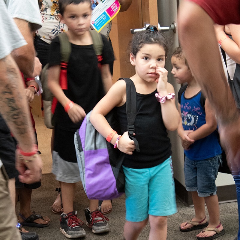 Young girl with a purple backpack waiting in line with other kids at the backpack drive