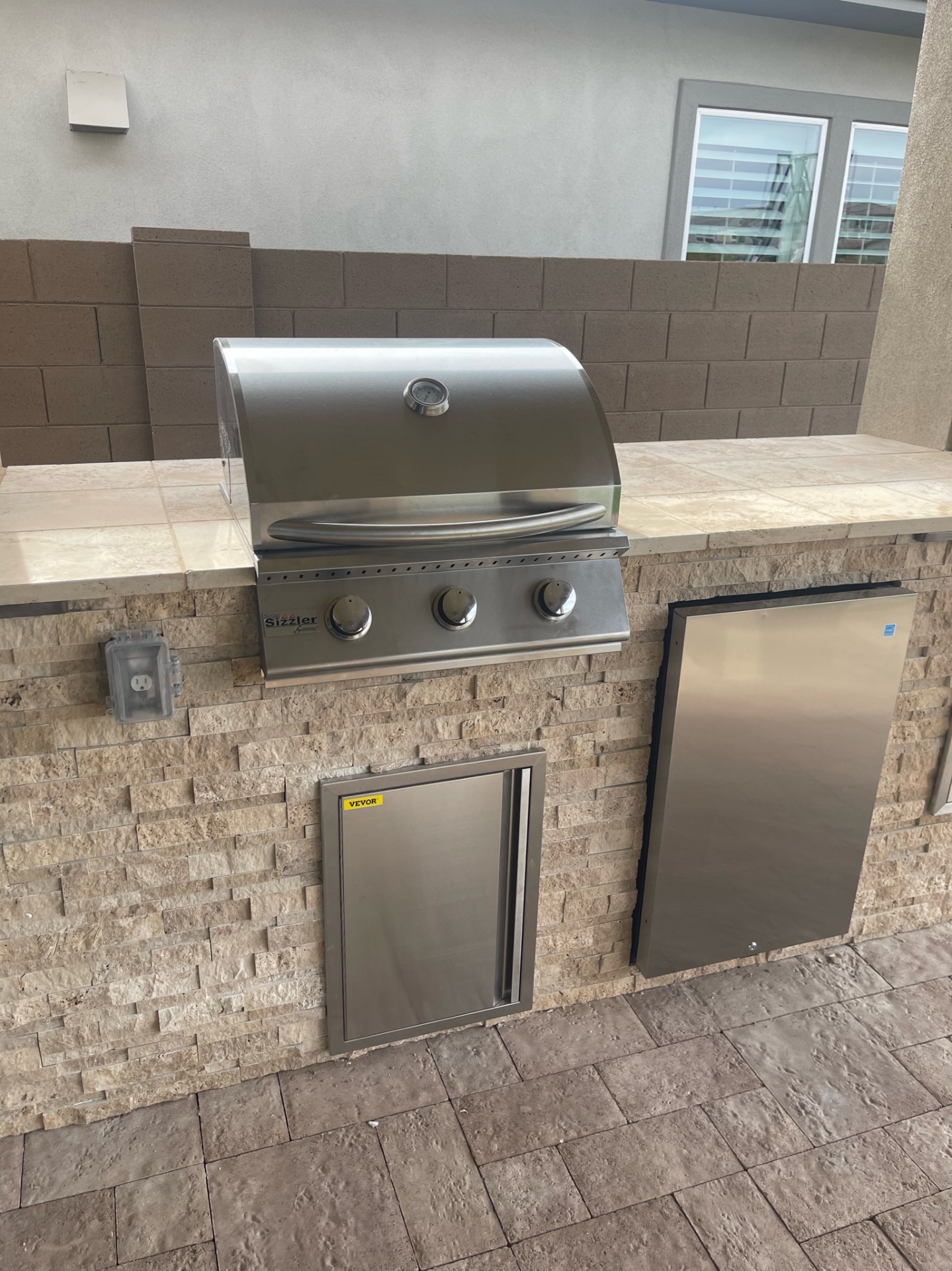 Peoria stacked-stone outdoor kitchen island with travertine bar top, built-in Sizzler grill, beverage fridge and stainless access door