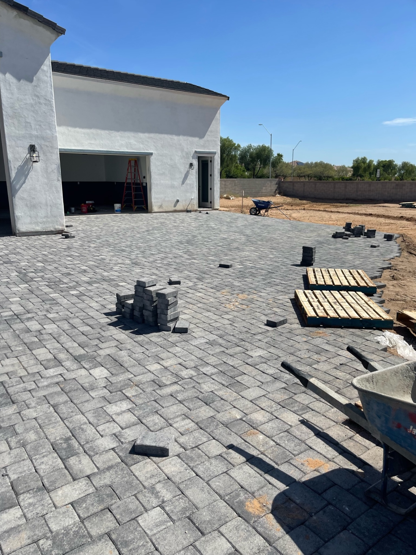 Waddell (Surprise-area) expansive charcoal-blend paver rear patio in progress with curved soldier-course edge transitioning toward the open lot behind a detached RV garage by AE Outdoor Living