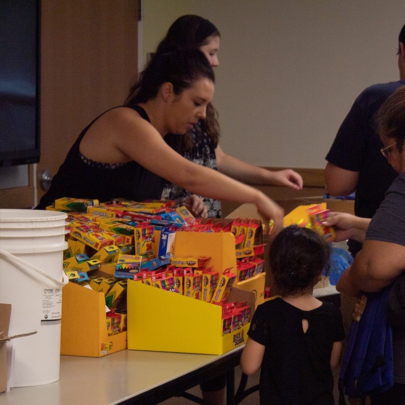 Volunteer sorting boxes of crayons at a supply table during the backpack drive