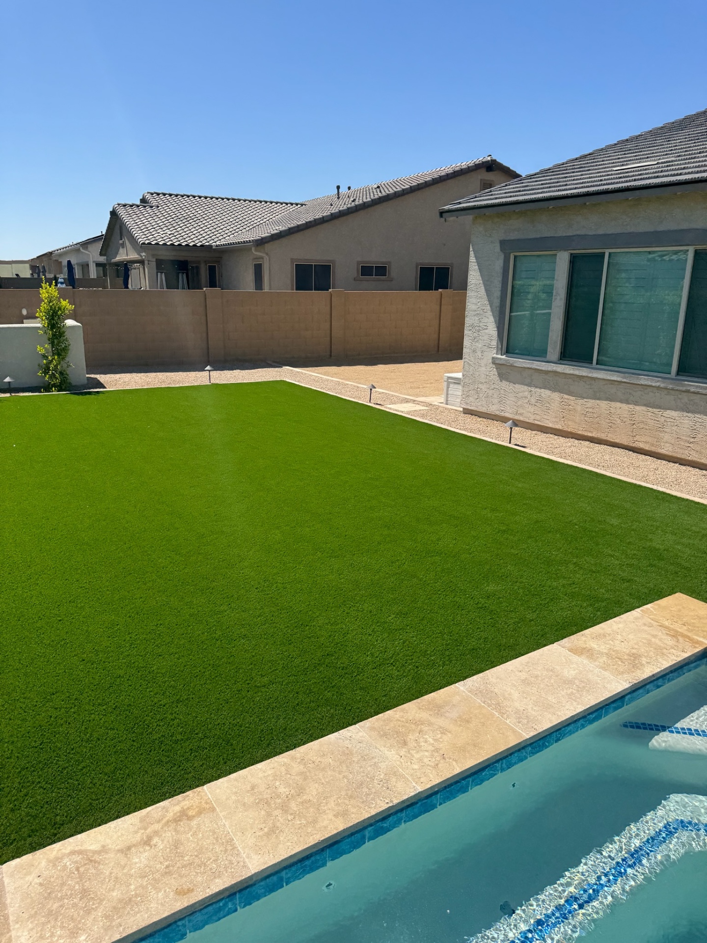 Peoria backyard artificial turf lawn poolside with travertine paver coping and low-voltage path lights