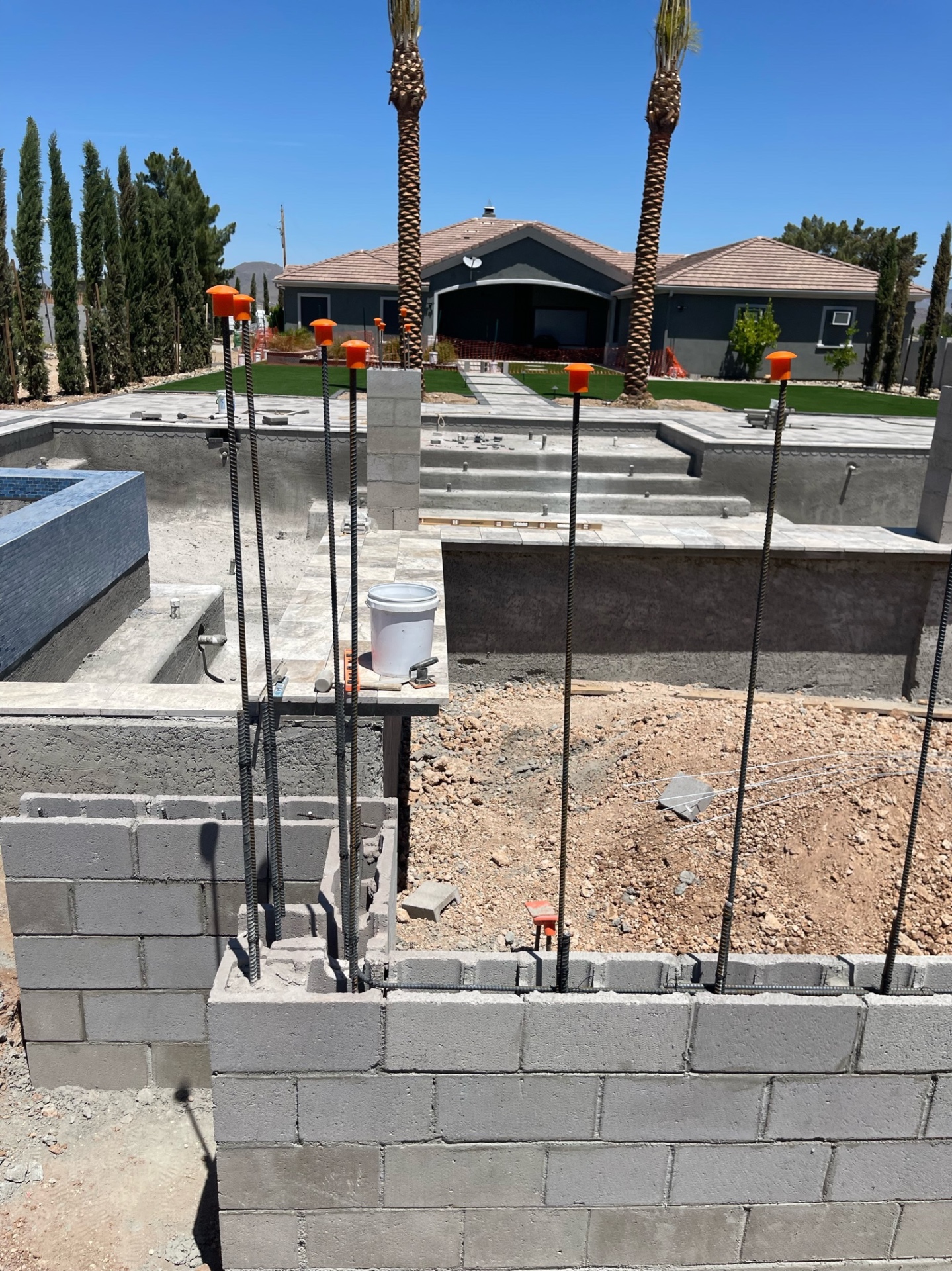 CMU wall under construction in front of a gunite pool shell and finished lawn beyond
