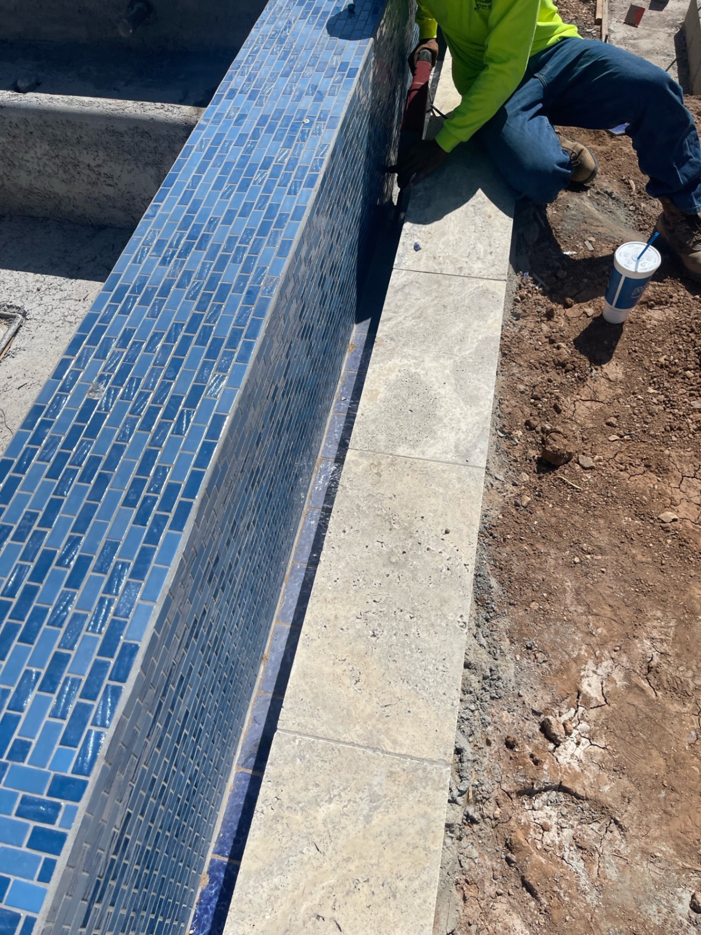 Close-up of blue glass spa tile and light stone coping with AE crew member working along the outside edge