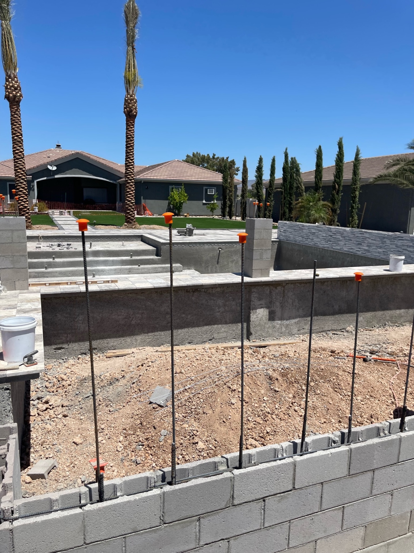 Pool shell with travertine-capped walls, raised spa with stacked-stone veneer, and rebar standing in adjacent footing
