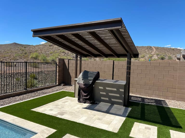 Bronze louvered aluminum cantilevered cover over a paver-and-turf BBQ zone with mountain backdrop.