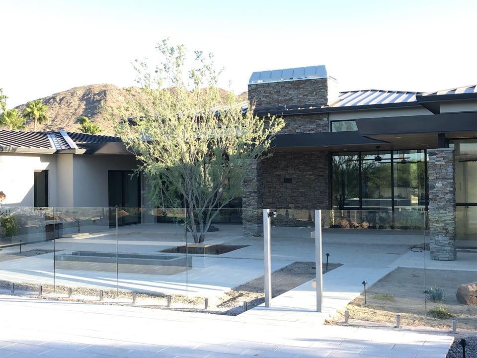 Modern home architecture and covered patio behind clear frameless glass fence panels around the pool area.