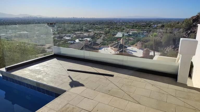 Glass railing panel photographed during installation on a hillside balcony overlooking Phoenix at midday.