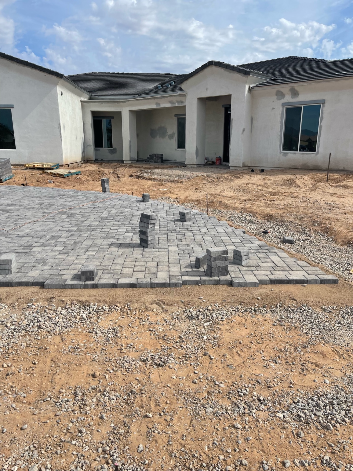 Waddell (Surprise-area) large paver patio at rear of tile-roof stucco home with soldier-course edging and stacked bundles for continued install by AE Outdoor Living