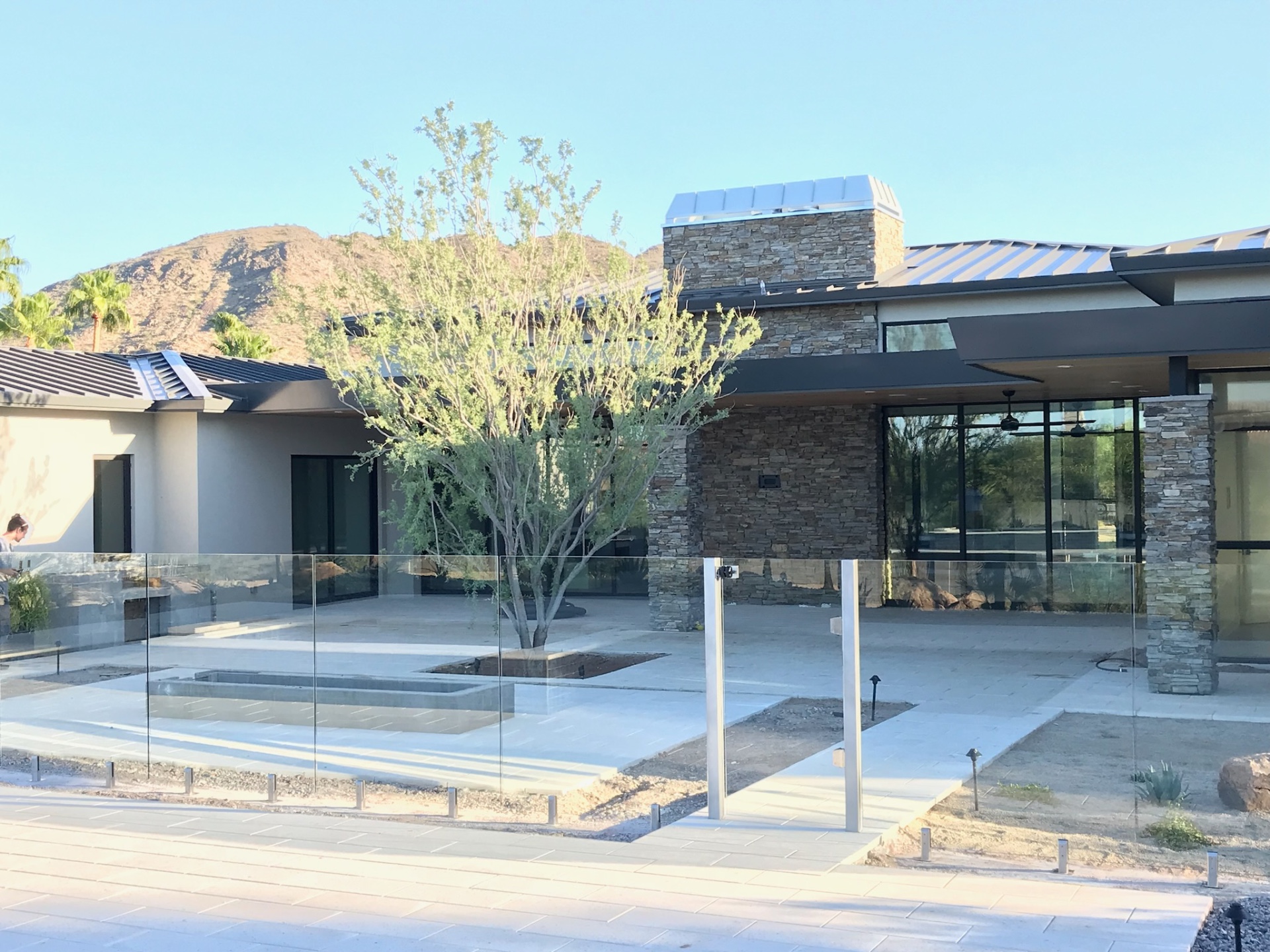 View across porcelain pavers framing the custom home patio, outdoor living space, and code-compliant frameless glass pool barrier.