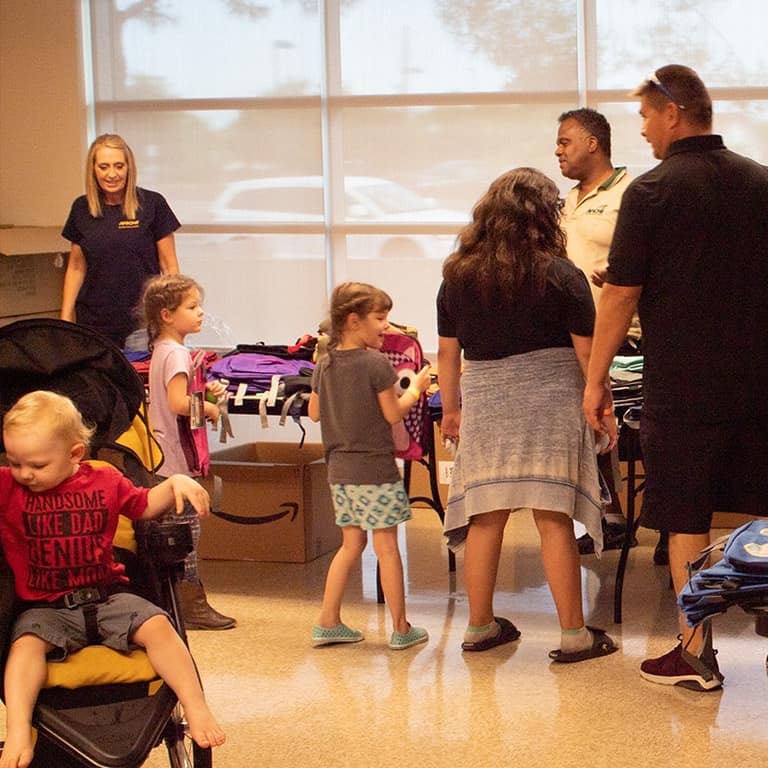 Families and volunteers moving through the backpack pickup area indoors