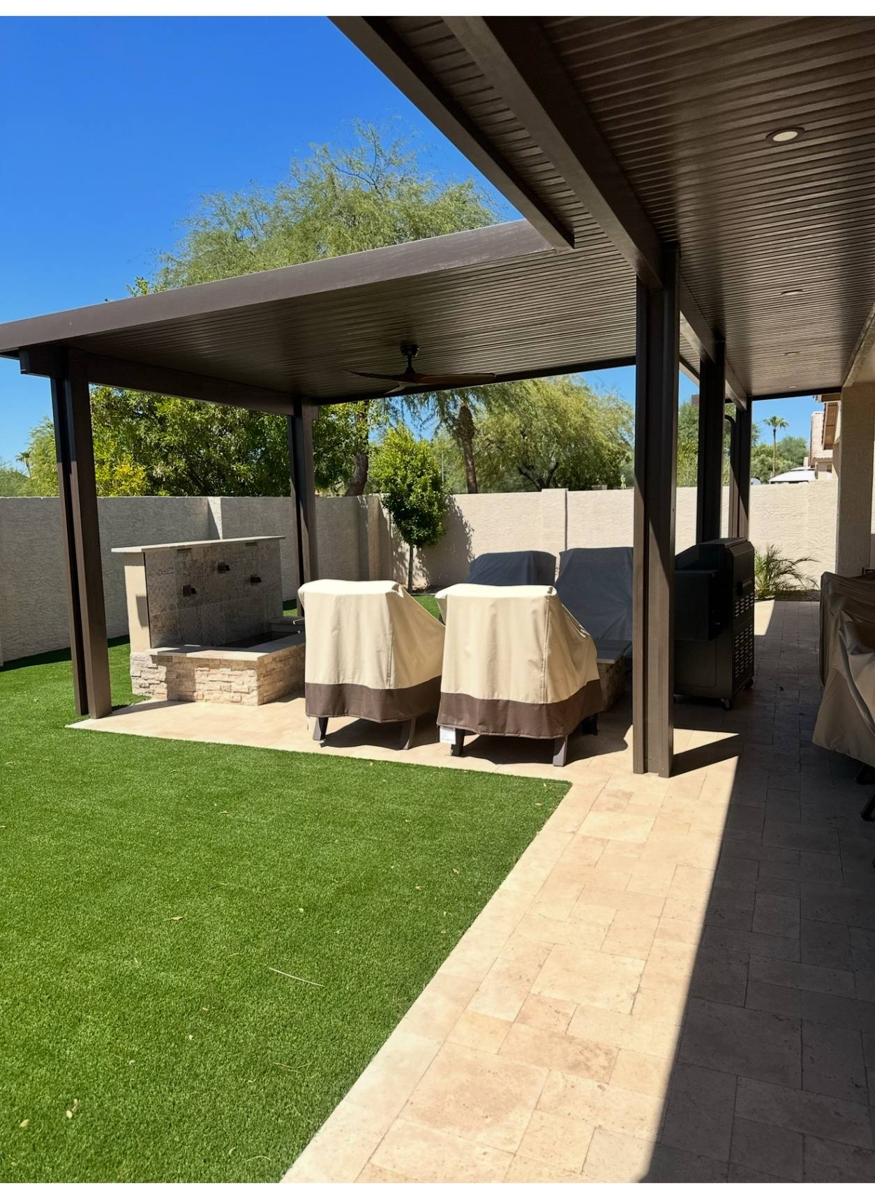 Solid-roof lounge pergola tying together fire feature, turf, and travertine-style paving.