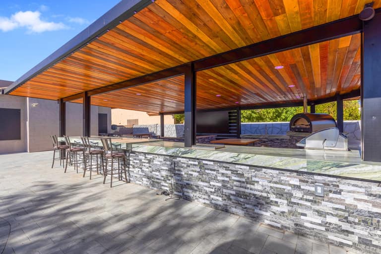 Covered outdoor living pavilion with a long stone-finished bar and cooking area in Litchfield Park.