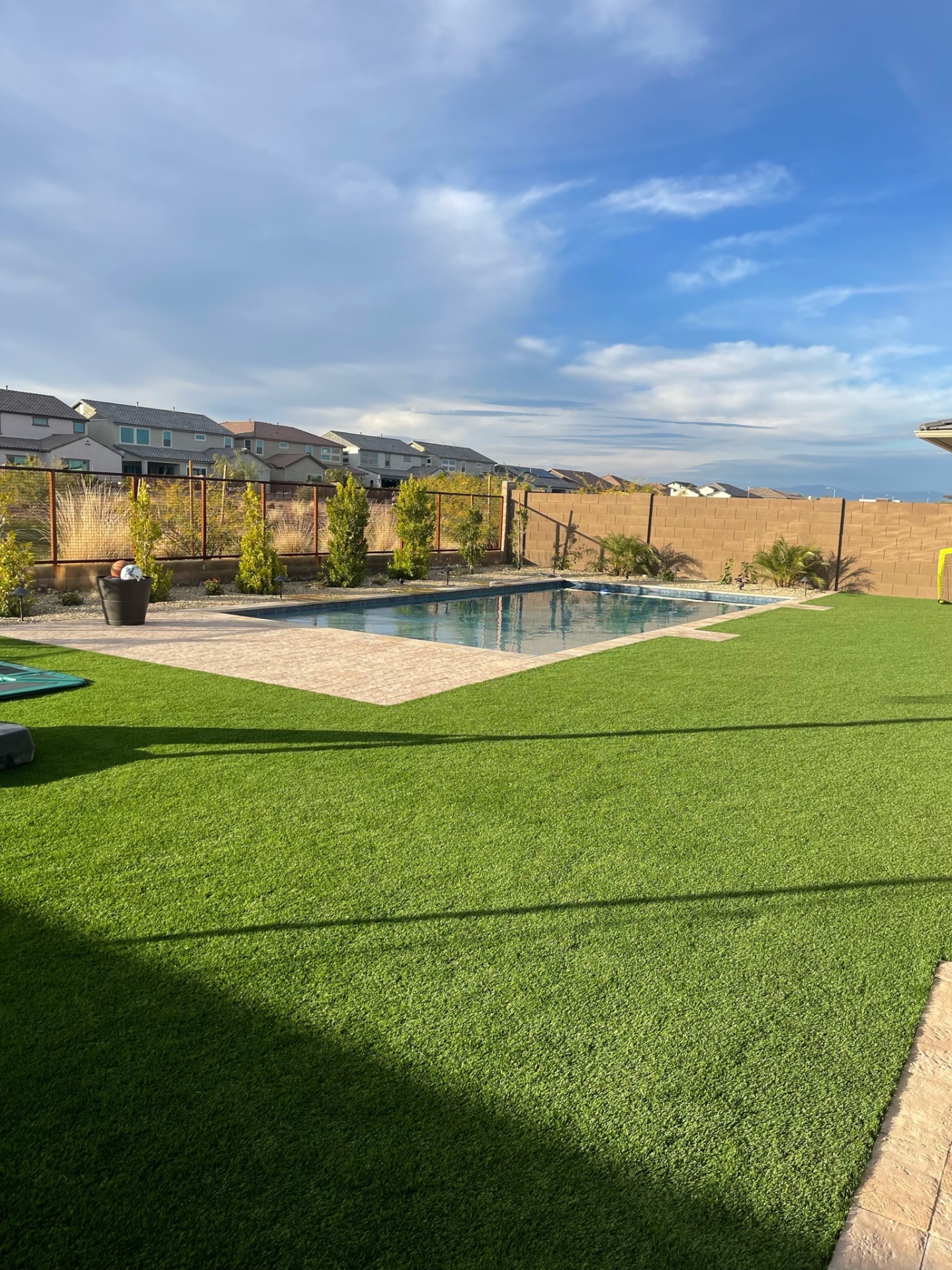Peoria rectangular pool with travertine paver deck, artificial turf lawn, iron view fence and desert-community skyline by AE Outdoor Living