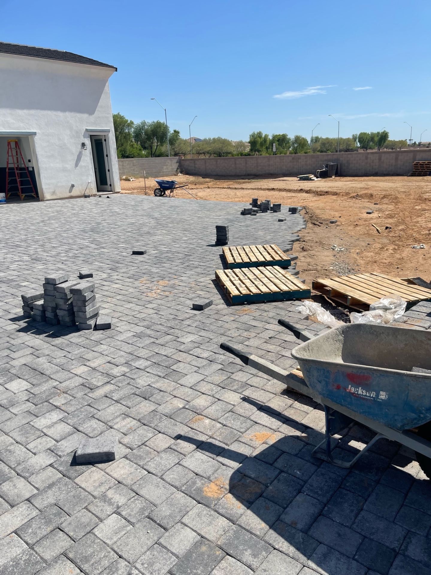 Waddell (Surprise-area) wide charcoal paver patio field with curved perimeter edging and staged pallets at the backyard buildout by AE Outdoor Living