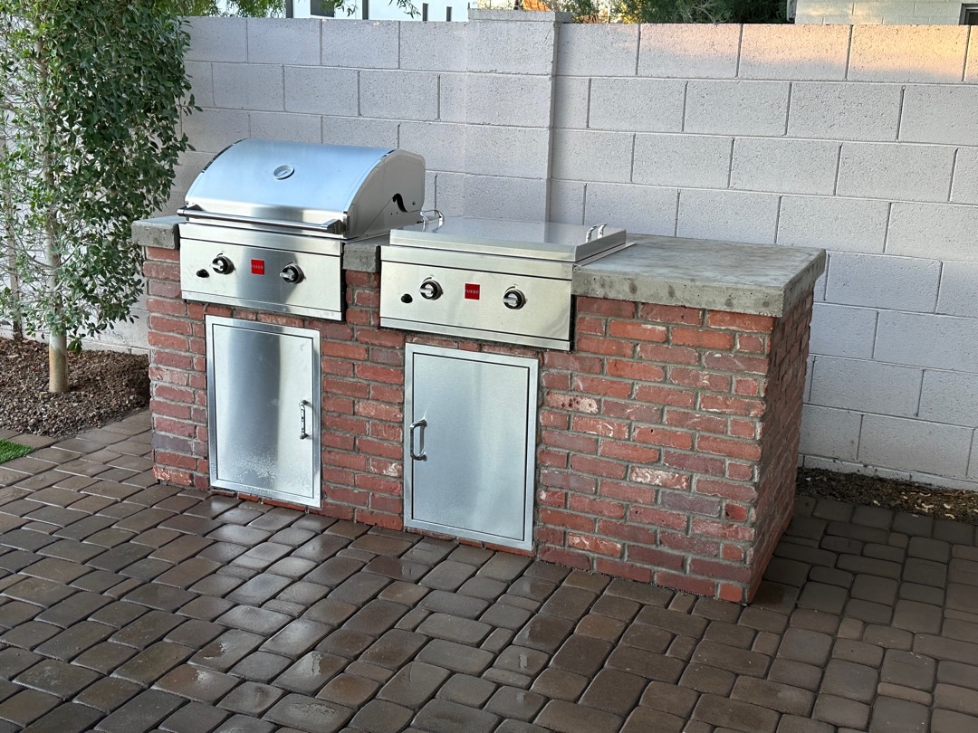Built-in outdoor kitchen with BBQ island, stone veneer, counter, storage, and low-voltage lighting
