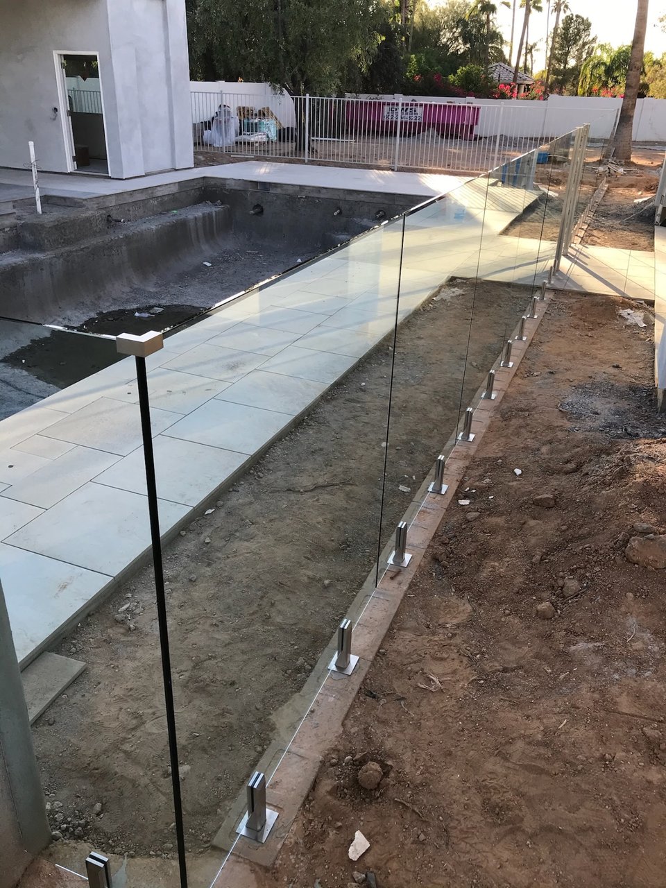 Frameless glass fence following the pool deck edge on spigots, viewed from inside the enclosed area.