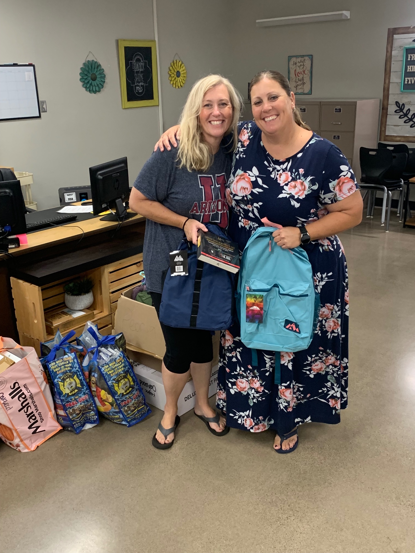 Two Peoria educators smiling and holding donated backpacks for their classrooms