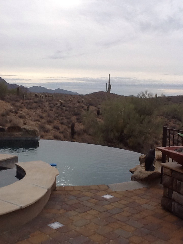 Fountain Hills negative-edge infinity pool at sunset with boulder waterfall wall, paver deck and unbroken McDowell Mountain view