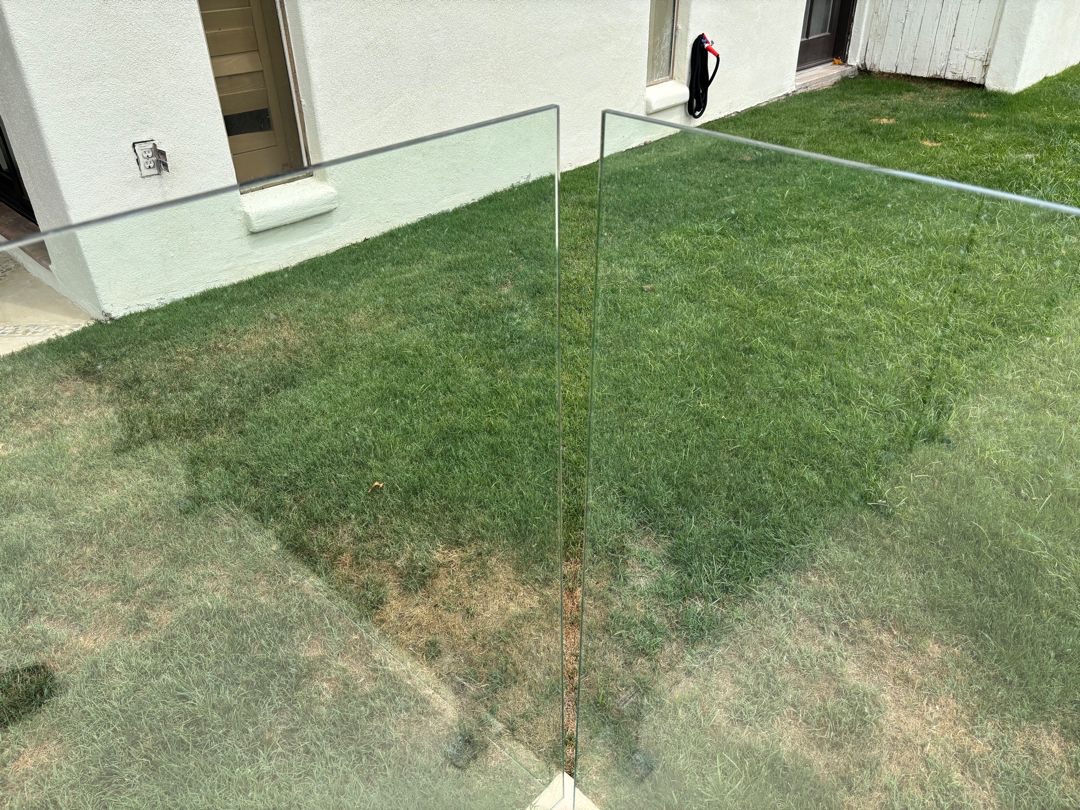 Two adjacent frameless glass barrier panels with visible variation in top-edge height.