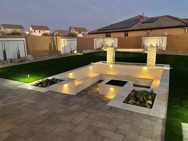Goodyear backyard sunken paver firepit lounge with travertine seat walls, artificial turf lawn and putting green by AE Outdoor Living