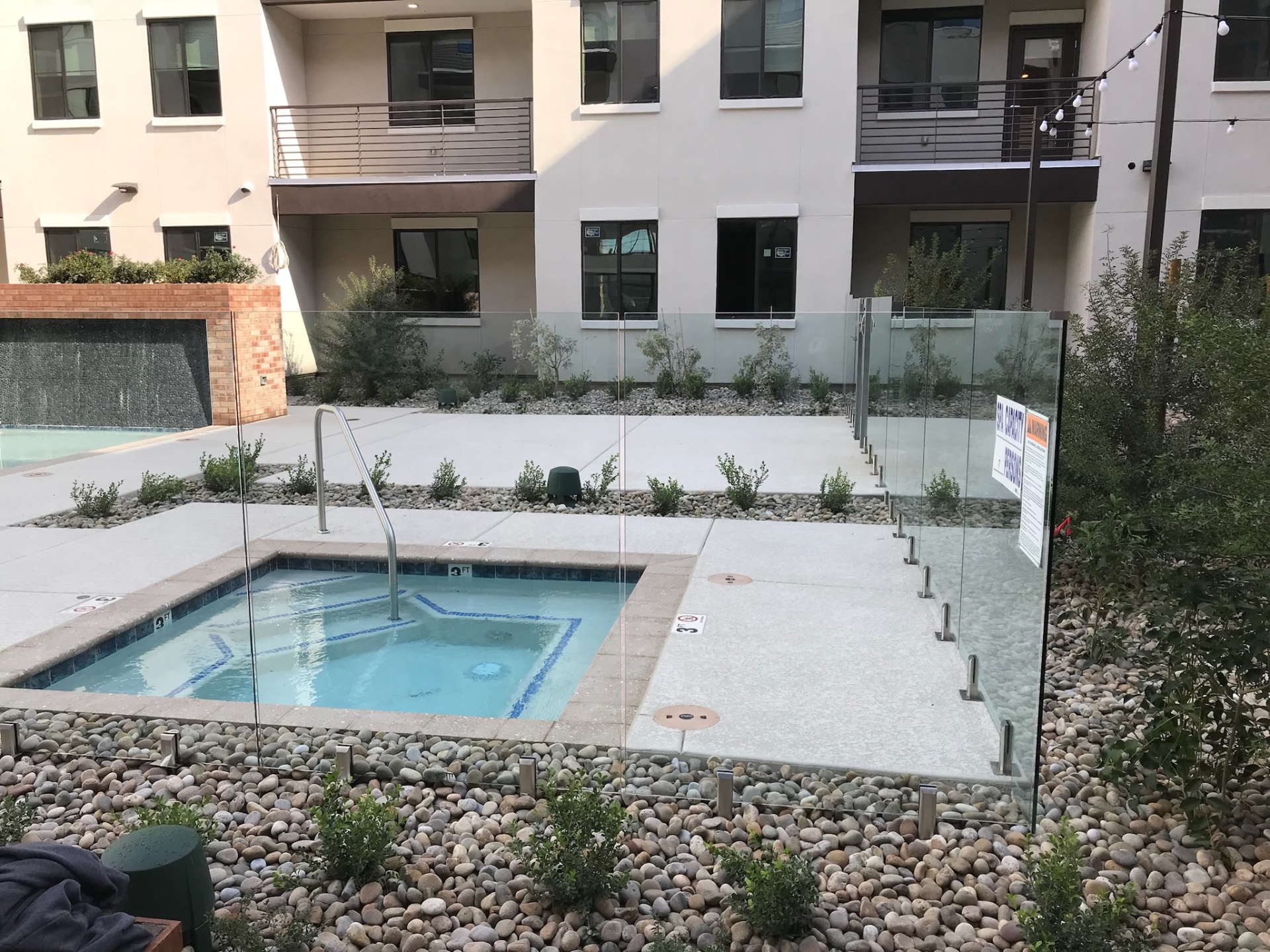 Commercial frameless glass fence protecting a spa and pool deck at an apartment community with clear sightlines across the amenity court.