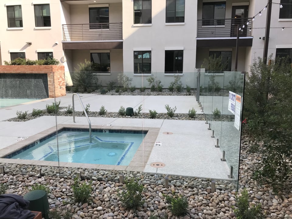 Frameless glass fence panels along a spa and pool deck at an apartment community, with open sightlines across the amenity court.