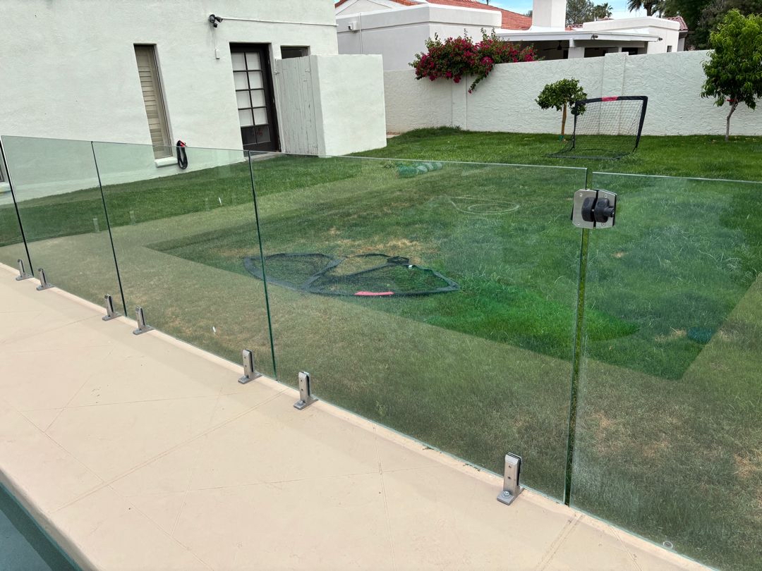Frameless glass pool barrier with stainless base-plate spigots visible at a decorative concrete pool deck surface in Phoenix.