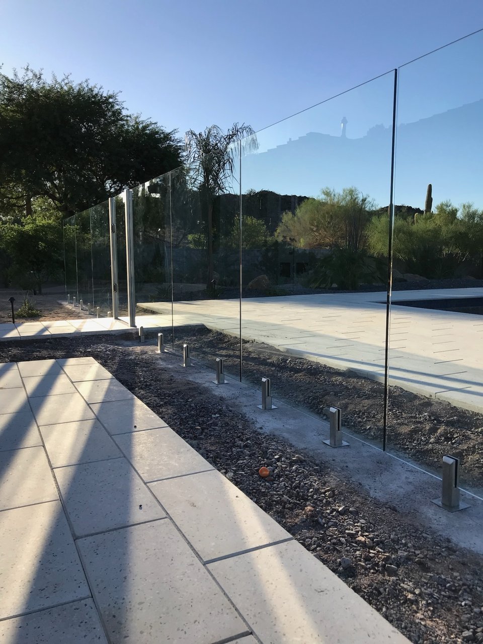 Long run of glass fence panels reflecting the deep blue sky and surrounding foothill landscape.