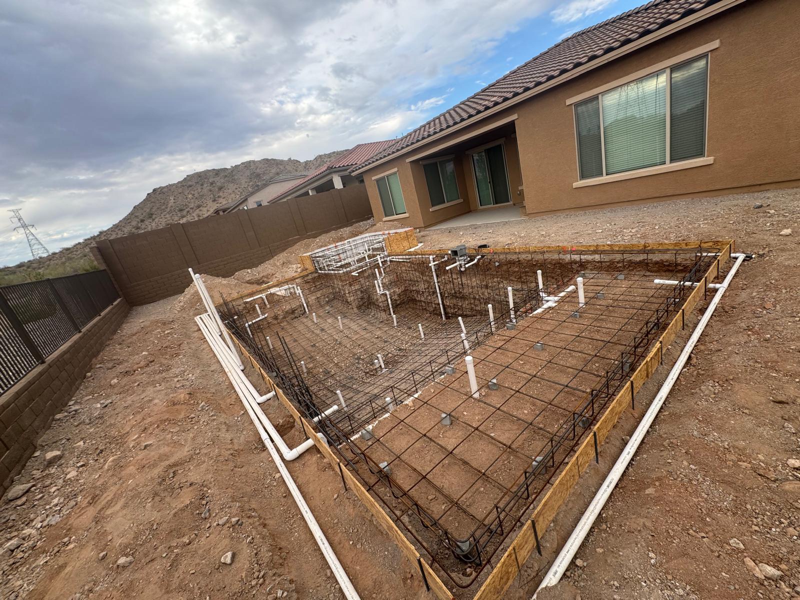 Engineered rebar cage and pool plumbing rough-in on a new build with mountain-view backdrop.