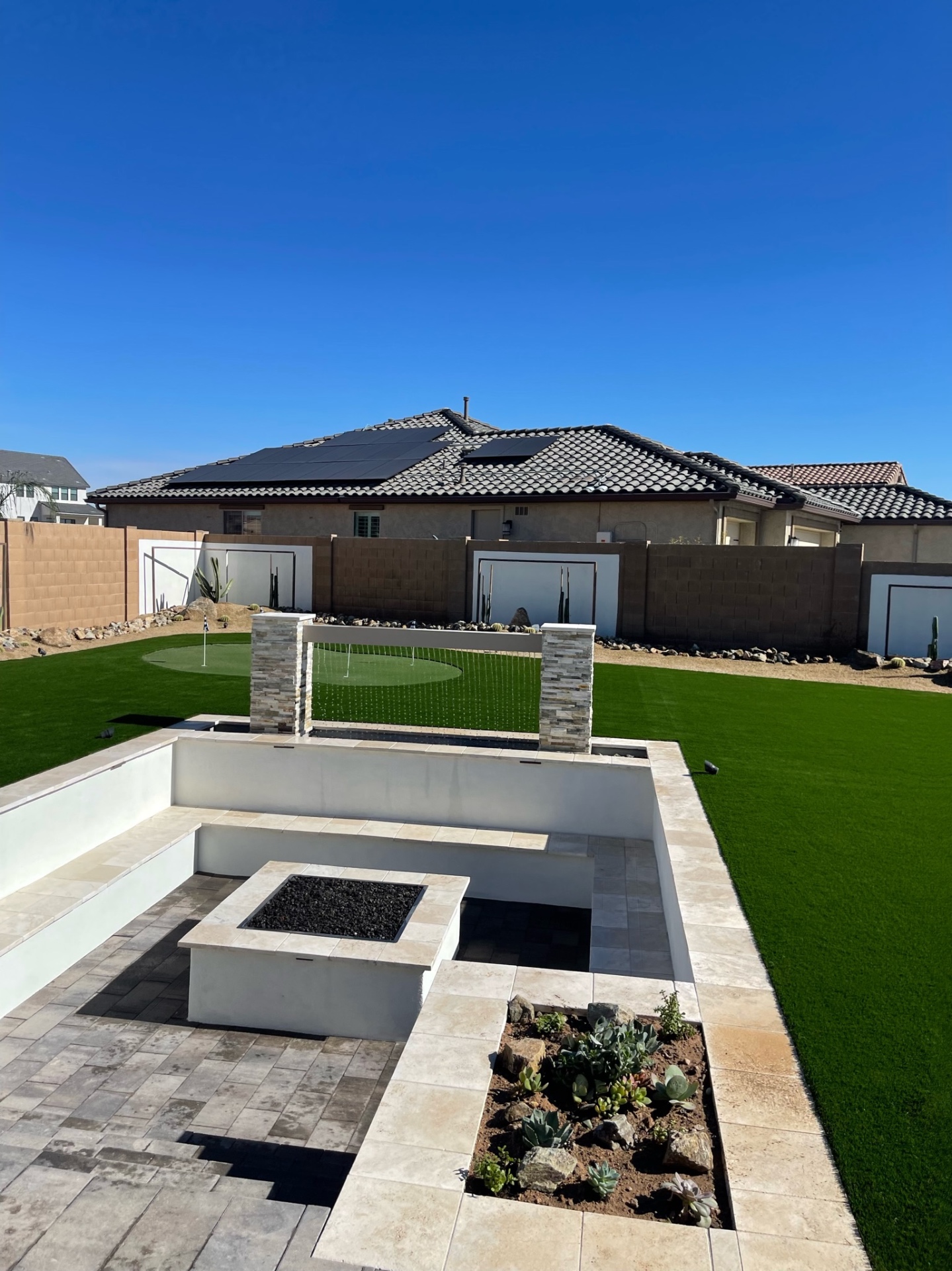 Goodyear sunken travertine firepit lounge, stacked-stone rain-curtain water feature, artificial putting green and succulent planter