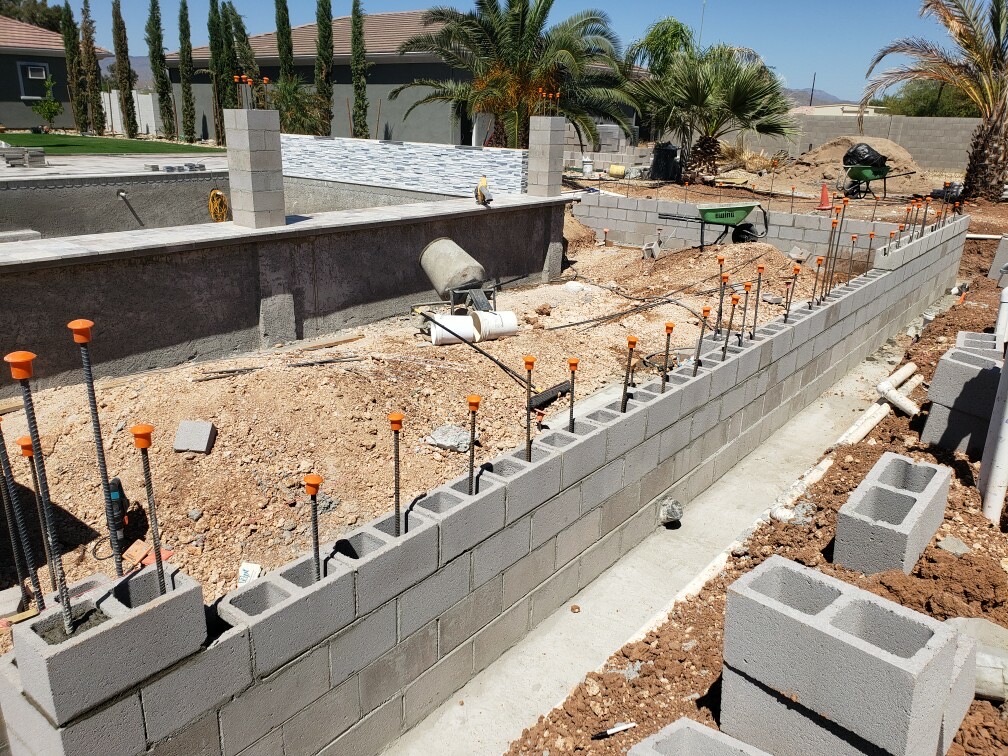 CMU block wall under construction along a pool with mosaic-tiled spa wall behind it