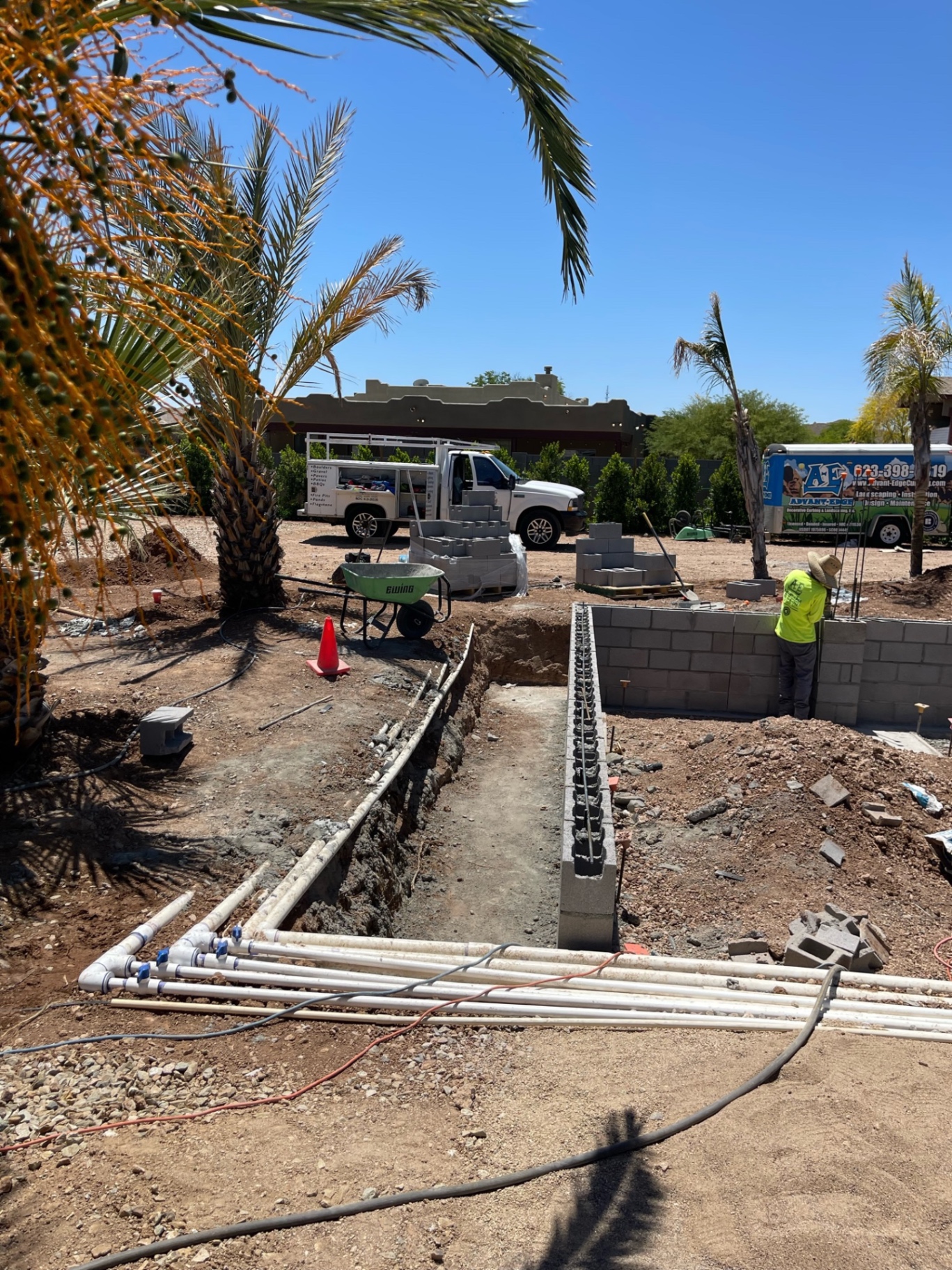 AE Advant-Edge work truck on jobsite with trenched footings, palms, and crew member tying rebar into a fresh block wall