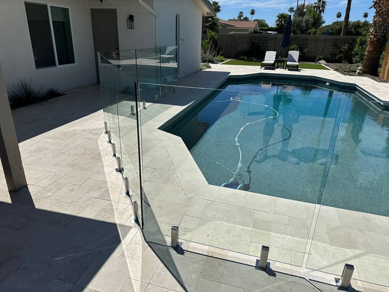 Frameless glass pool fence returning into a Scottsdale home's exterior wall with stainless surface-mount spigots