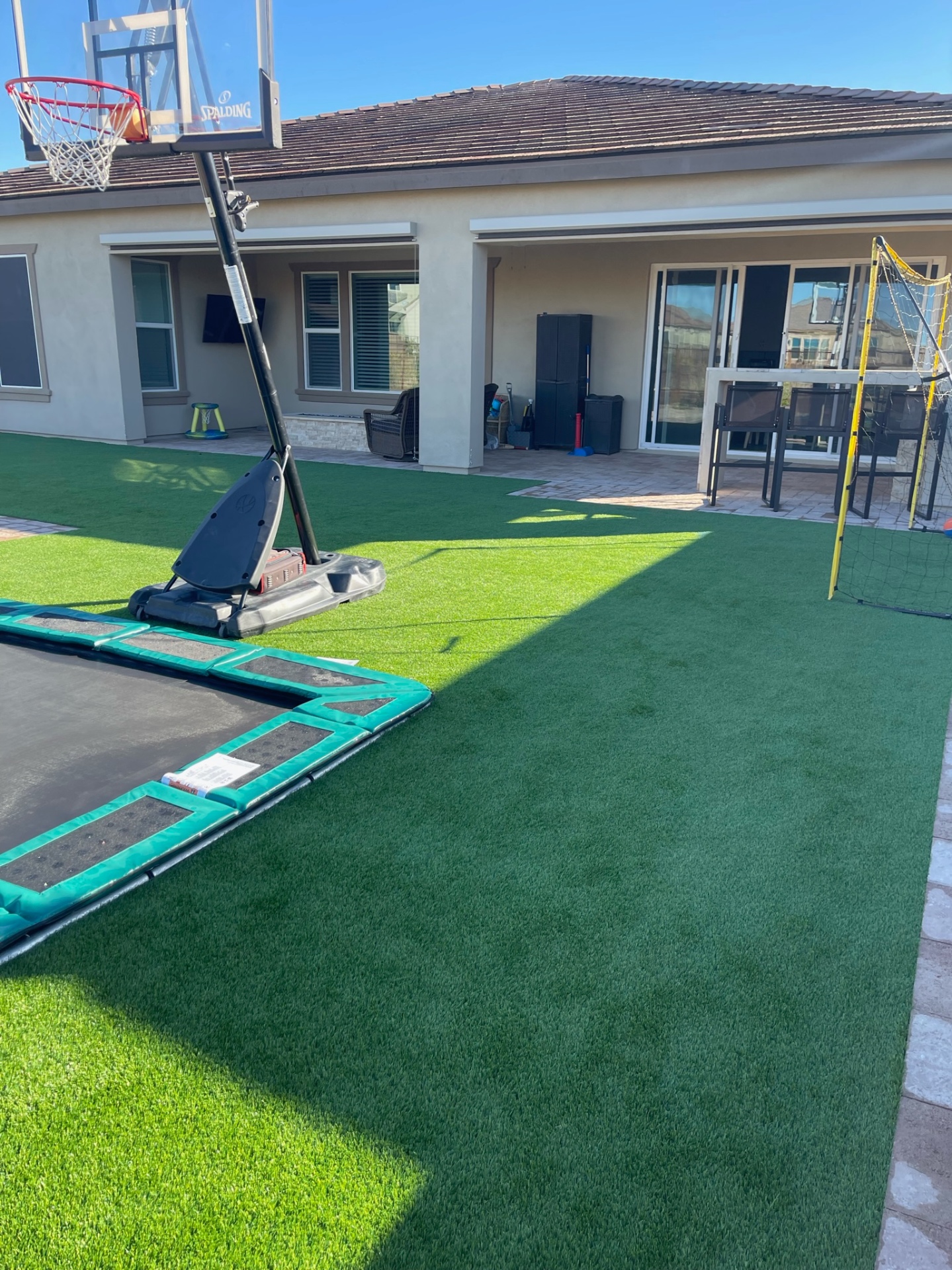 Peoria full artificial turf sport lawn with in-ground trampoline, portable basketball hoop and paver patio at rear of home by AE Outdoor Living