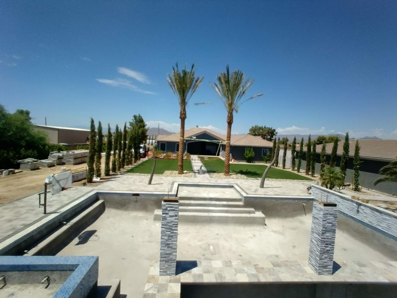 Sweeping overview of completed paver deck, pool shell, raised spa, and landscaped backyard with palms and cypress trees