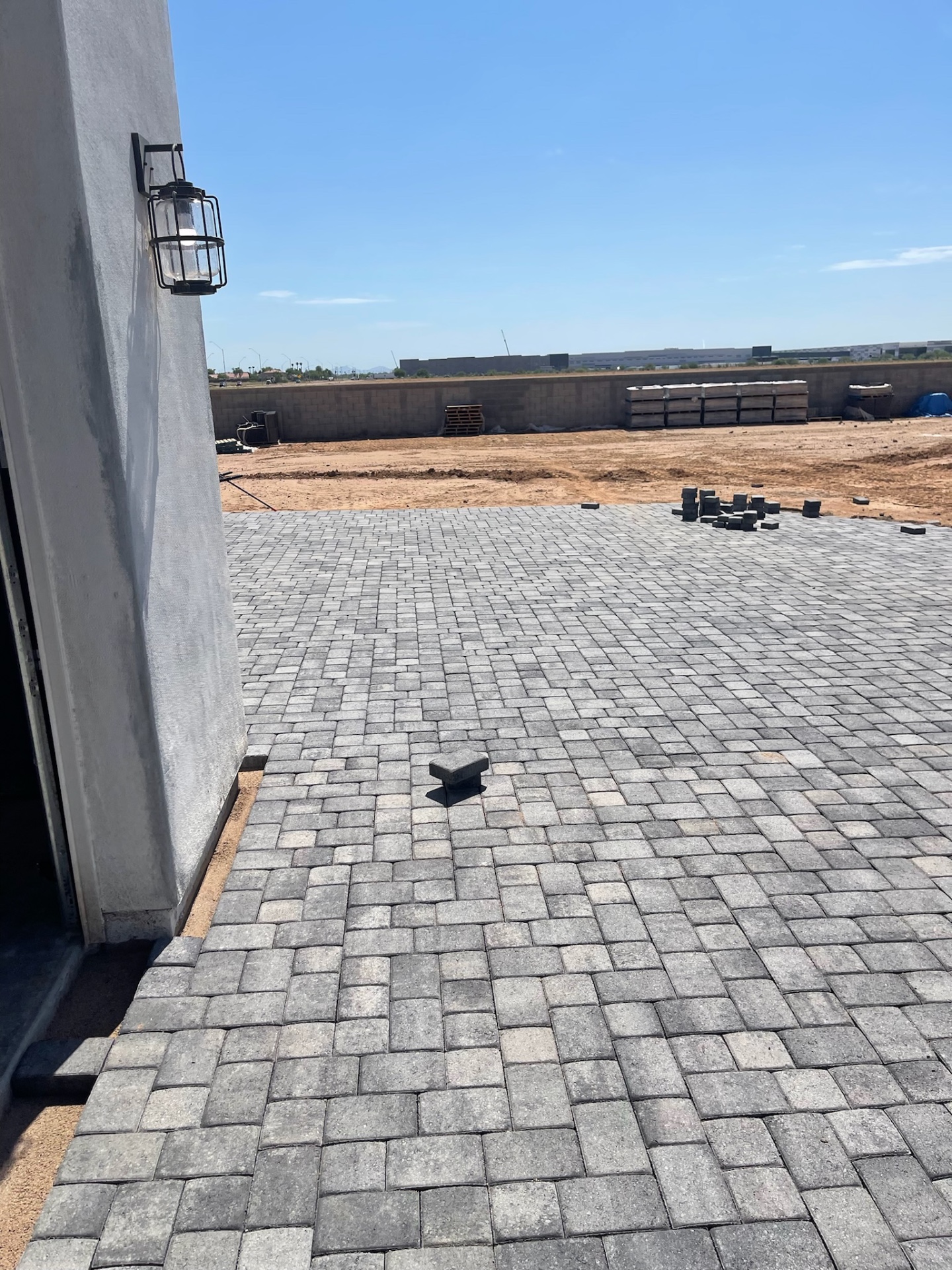 Waddell (Surprise-area) rear patio charcoal paver field extending from the home toward the open backyard lot with staged bundles along the far wall by AE Outdoor Living