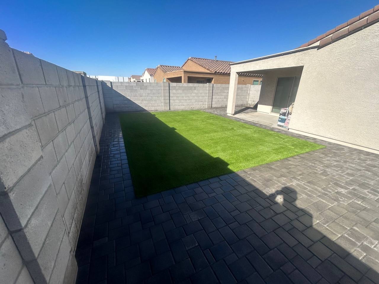 Wide-angle compact backyard with artificial turf rectangle and charcoal paver wrap