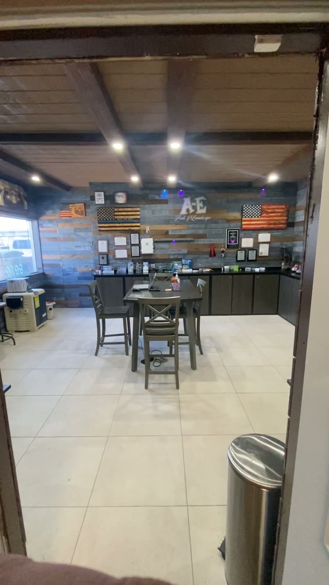 The design table inside the AE Outdoor Living showroom in Peoria, Arizona, with the reclaimed-wood credenza wall of framed licenses and certifications behind it.