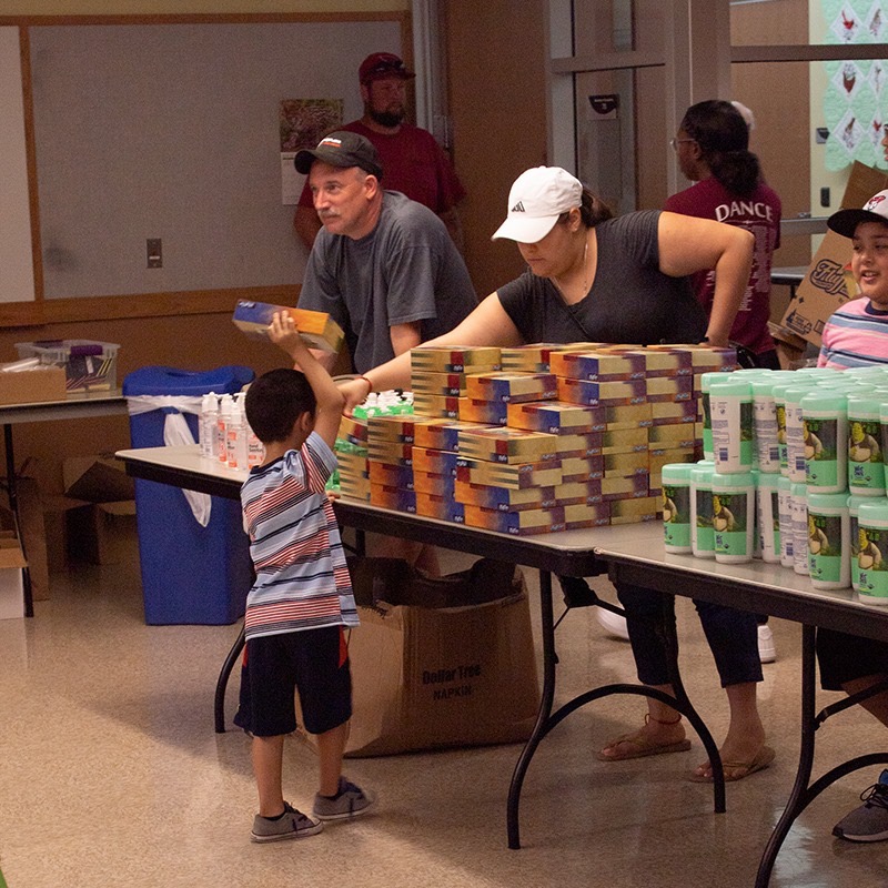 Volunteers handing out tissues and cleaning supplies to a young boy at the supply table