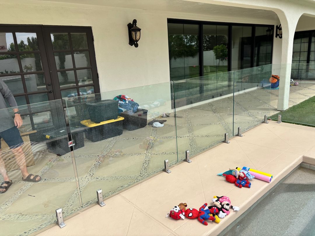 Long run of frameless glass barrier panels with base plates visible at a diamond-pattern paver finish surface.