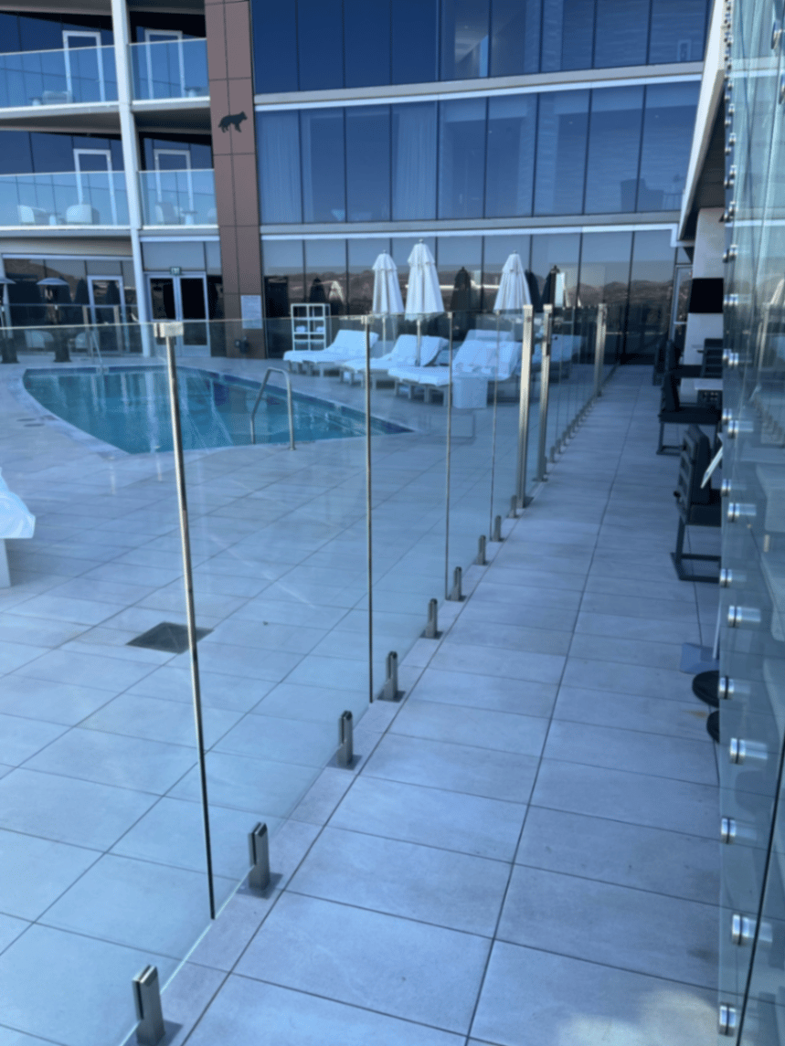 Frameless glass pool perimeter on a Scottsdale hotel deck with stainless surface-mount spigots into porcelain pavers