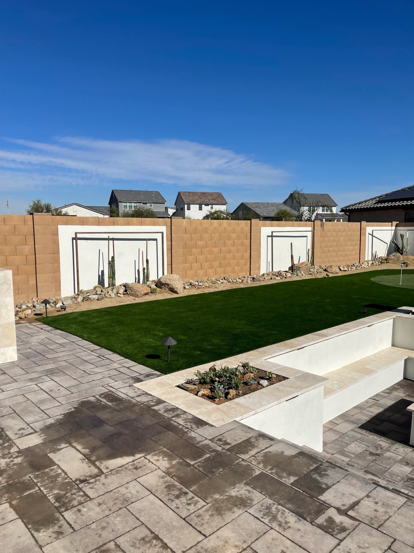Goodyear backyard artificial turf lawn with putting green, travertine bench with succulent planter and stucco privacy pilasters along block wall