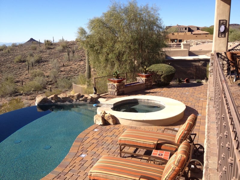 Fountain Hills infinity-edge pool with raised travertine spa, stacked-stone raised planter columns and paver pool deck with mountain and saguaro views