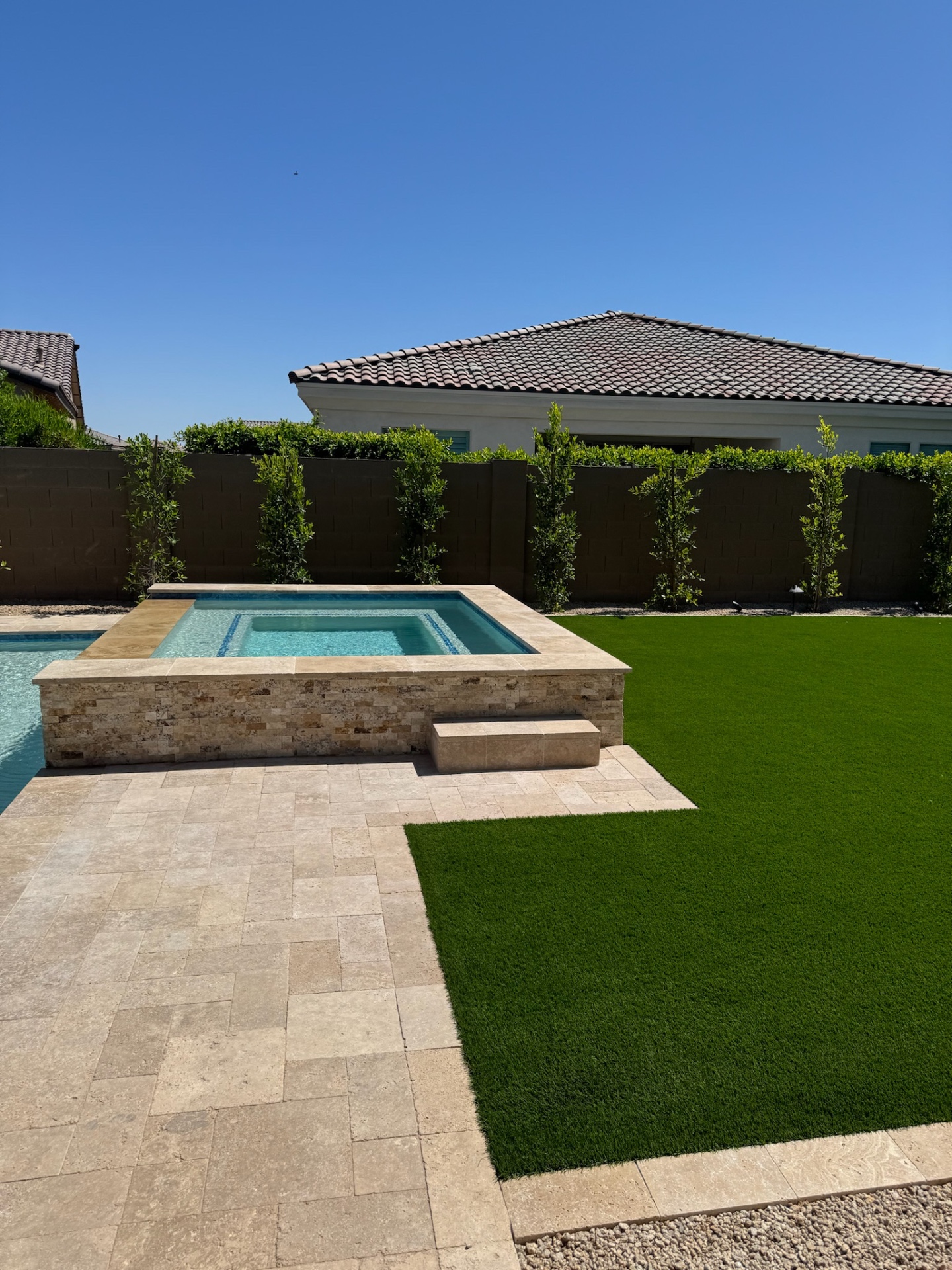 Peoria raised travertine spa with stacked-stone veneer next to a fresh artificial turf lawn