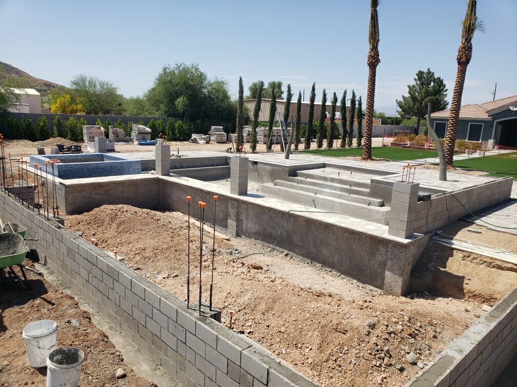 Wide view of pool shell with raised tiled spa, step risers, and full paver deck installed