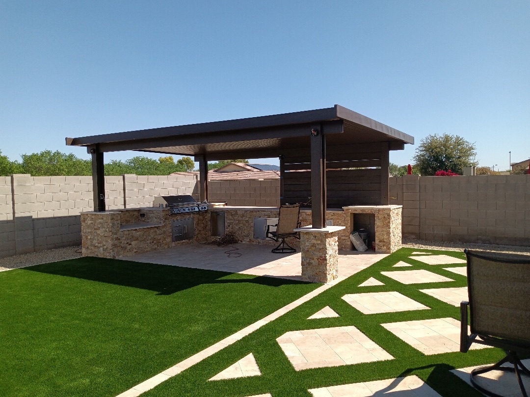 Outdoor kitchen under a pergola with turf and patterned hardscape tying the whole yard together.